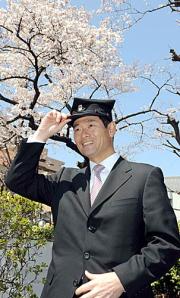 早大大学院の入学式後、桜を背に早大の学帽をかぶる桑田氏