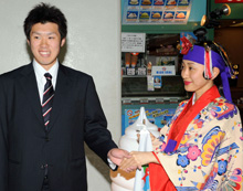 那覇空港に到着した佐藤由は、伝統衣装を着た観光スタッフの友利明菜さんから歓迎され照れる(撮影・栗山尚久)