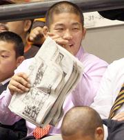 母校の応援をする石井慧は自身の記事が掲載された本紙を読み笑顔を見せた
