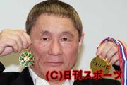 コマンドールの勲章とお手製の金メダルを手にポーズする北野武監督