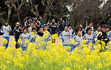 指宿合宿で菜の花が咲く敷地をランニングする日本代表選手と岡田監督（中央）