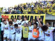 横手社長（左から５人目）を中心に喜び合う北九州イレブンとサポーター