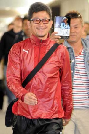 笑顔で帰国したカズ。後方はカズの本をかざす関係者（撮影・宮川勝也）