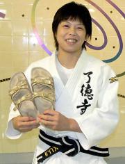 笑顔で金のサンダルを見せる福見