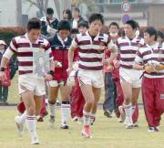 8月に急逝した石塚監督の遺影を抱いてベンチに戻る松本主将(左)
