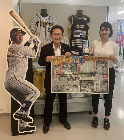 阪神近本のパネル、記念グッズ、30試合連続安打の記事が掲載された日刊スポーツと写真に納まる門康彦淡路市長（左）。右は同市スポーツ推進課の加藤美夏さん（撮影・中野椋）