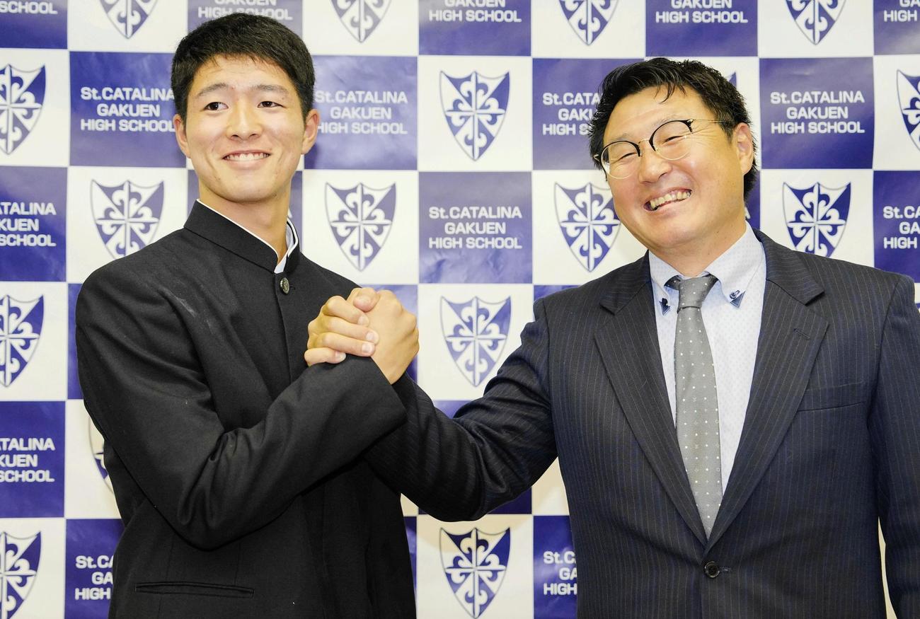 オリックスから2位指名を受け、聖カタリナ学園の浮田宏行監督（右）と笑顔で握手する河内康介（共同）