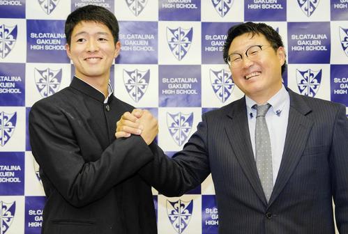 オリックスから2位指名を受け、聖カタリナ学園の浮田宏行監督（右）と笑顔で握手する河内康介（共同）