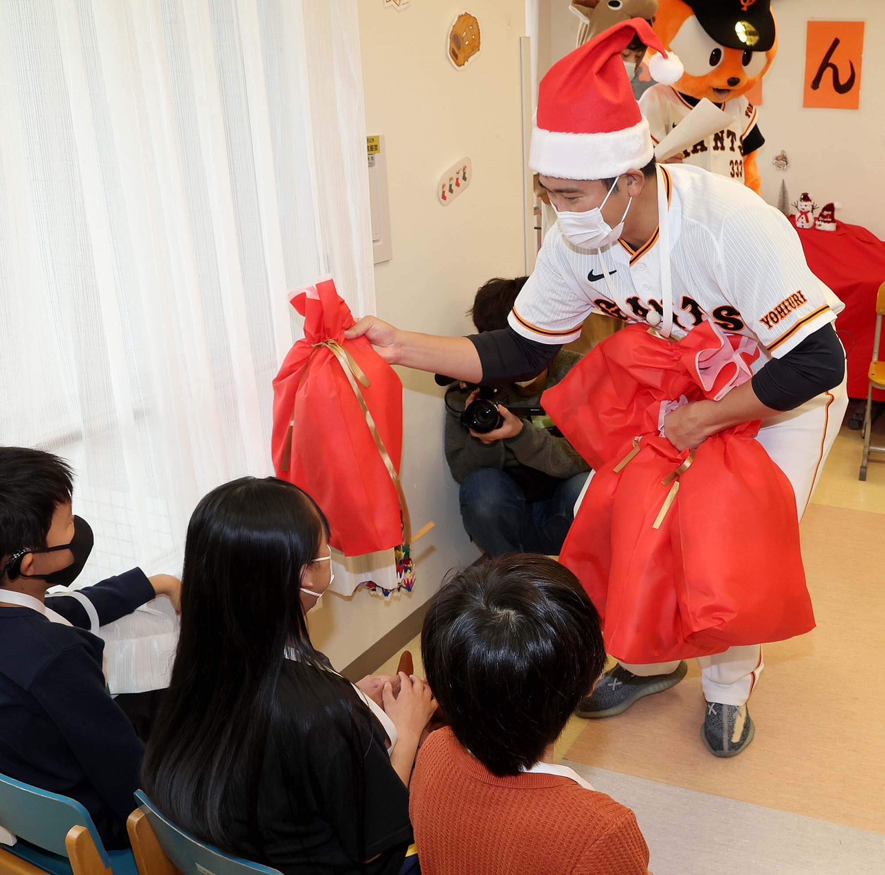 サンタクロースの帽子を被り、子供にプレゼントを渡す巨人菅野（球団提供）