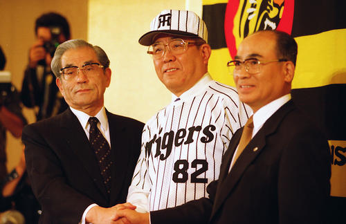 98年10月、阪神入団会見でユニホームに袖を通して笑顔を見せる監督の野村克也さん（中央）。左は久万オーナー、右は高田社長