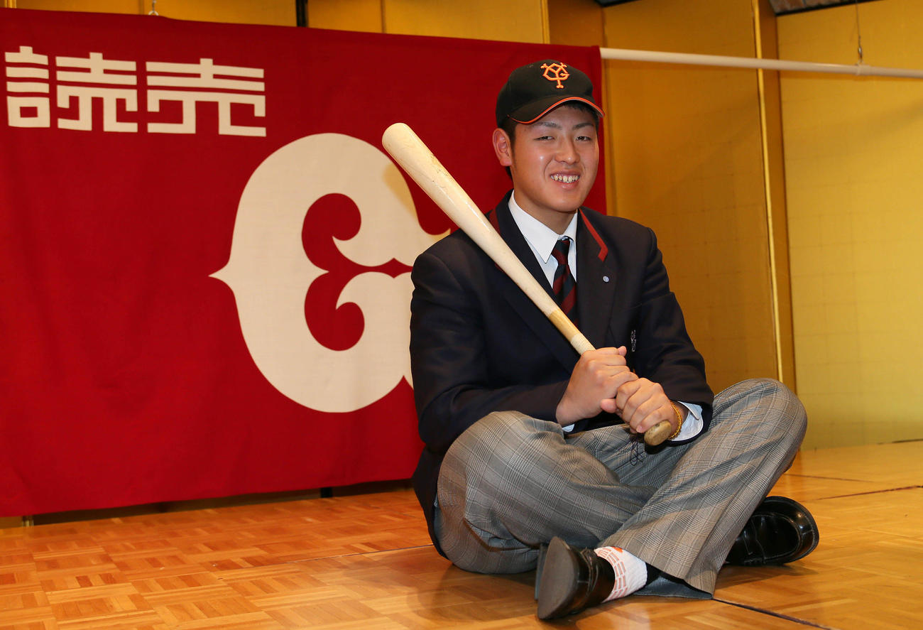 14年11月、巨人ドラフト1位の岡本は仮契約を終え球団旗を背に笑顔