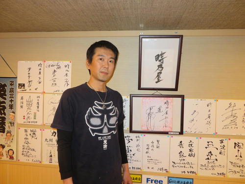 店内に掲げた数々のサインの前に立つ中村さん。中央の額に入った２つが、原辰徳氏から贈られたもの