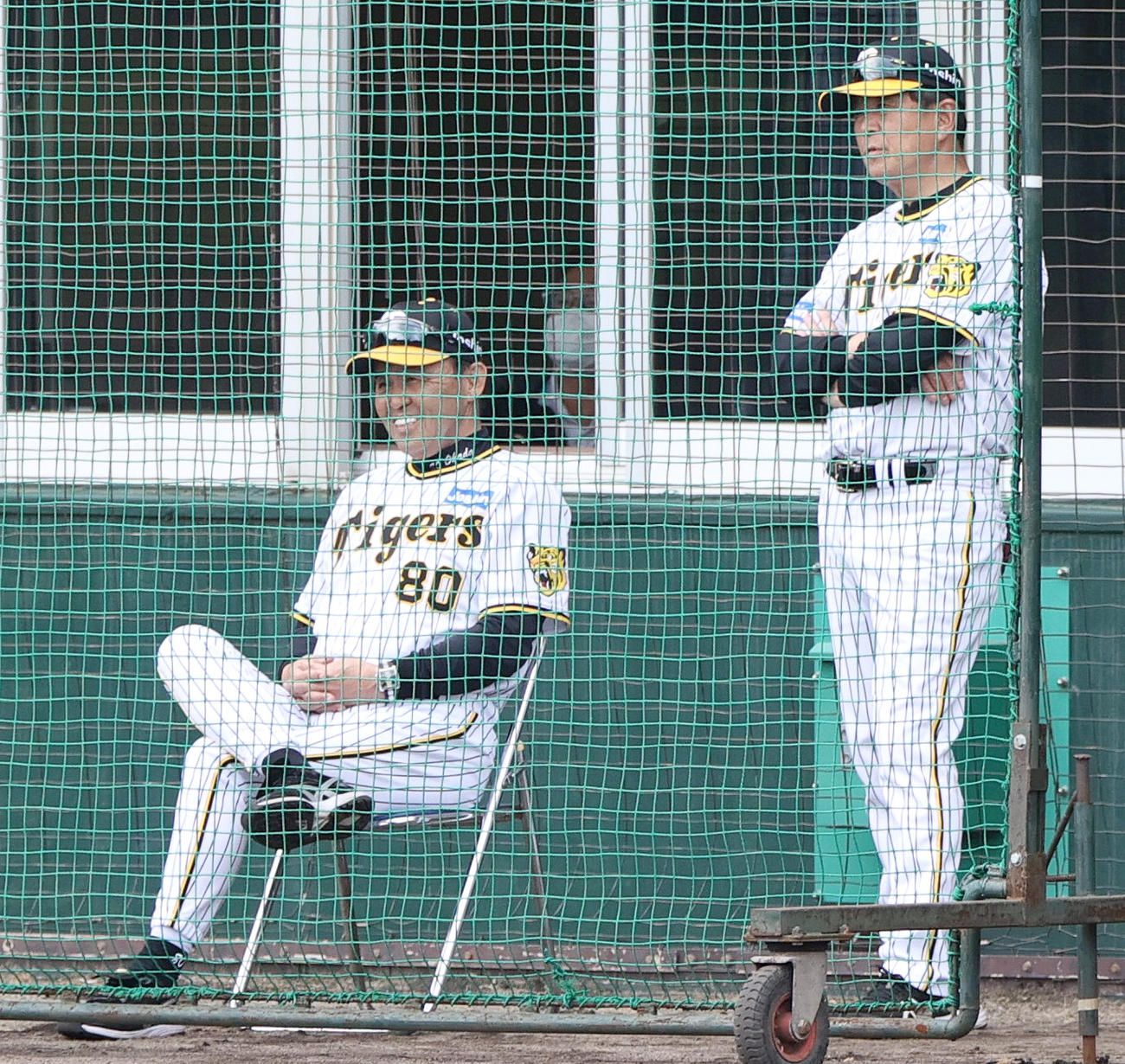 紅白戦　バックネット裏で笑顔を見せる岡田監督（左）と平田ヘッドコーチ（2023年2月12日撮影）