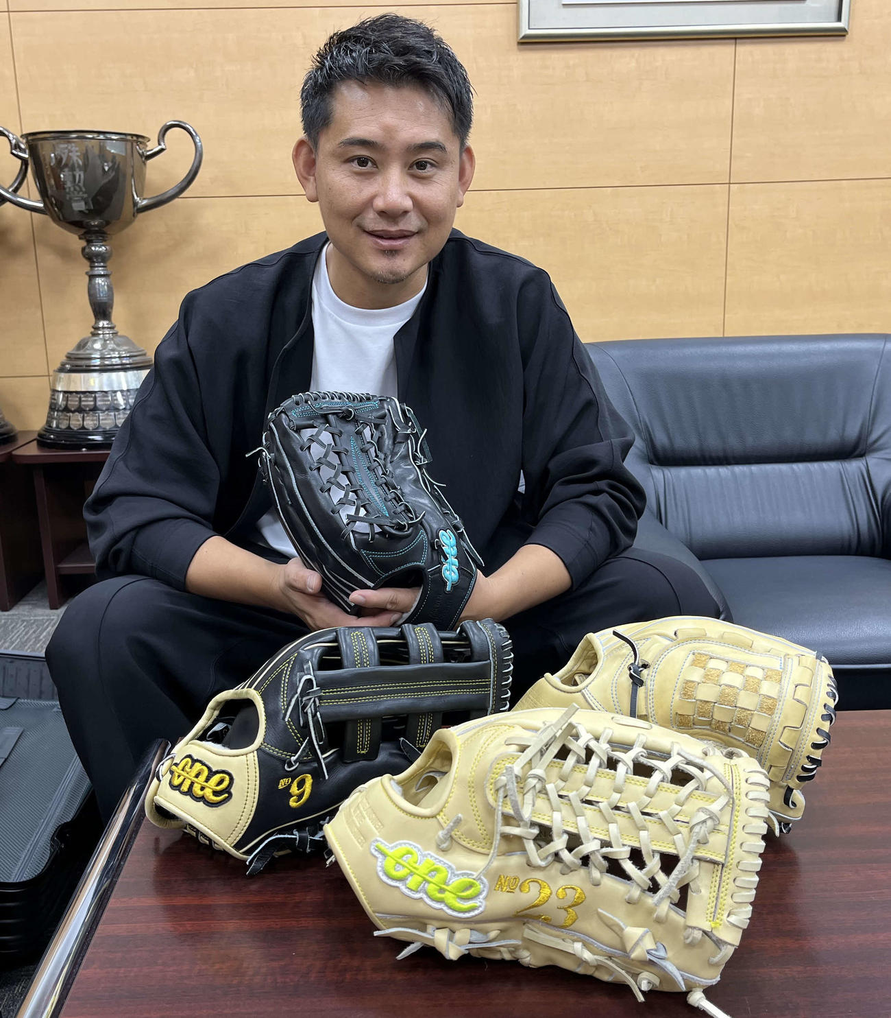 松坂恭平さんは自社で手がけたグラブ「ONE OF THE ANSWER」を手にした。机上の左が今季ソフトバンク柳田が使用、手前が巨人松田が使用したモデル（撮影・久我悟）