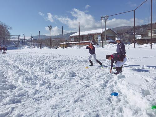 今年2月の雪に埋まったグラウンドで長靴を履いて練習する飯山ナイン（飯山高校野球部提供）