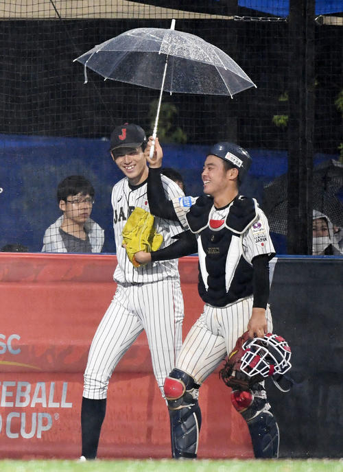 日本対パナマ　6回裏途中、雨で試合が中断し、ブルペンから傘を差しベンチへ戻る佐々木（左）と山瀬（撮影・横山健太）