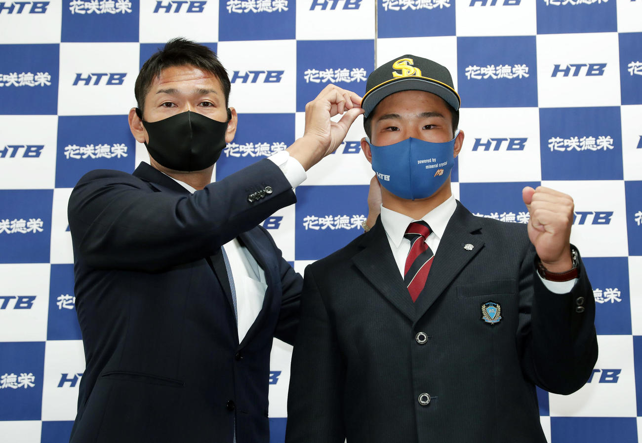 ソフトバンク永井編成育成本部長兼スカウト・育成部長（左）らの指名あいさつを受け、帽子をかぶせてもらいガッツポーズするドラフト1位の花咲徳栄・井上（撮影・前田充）