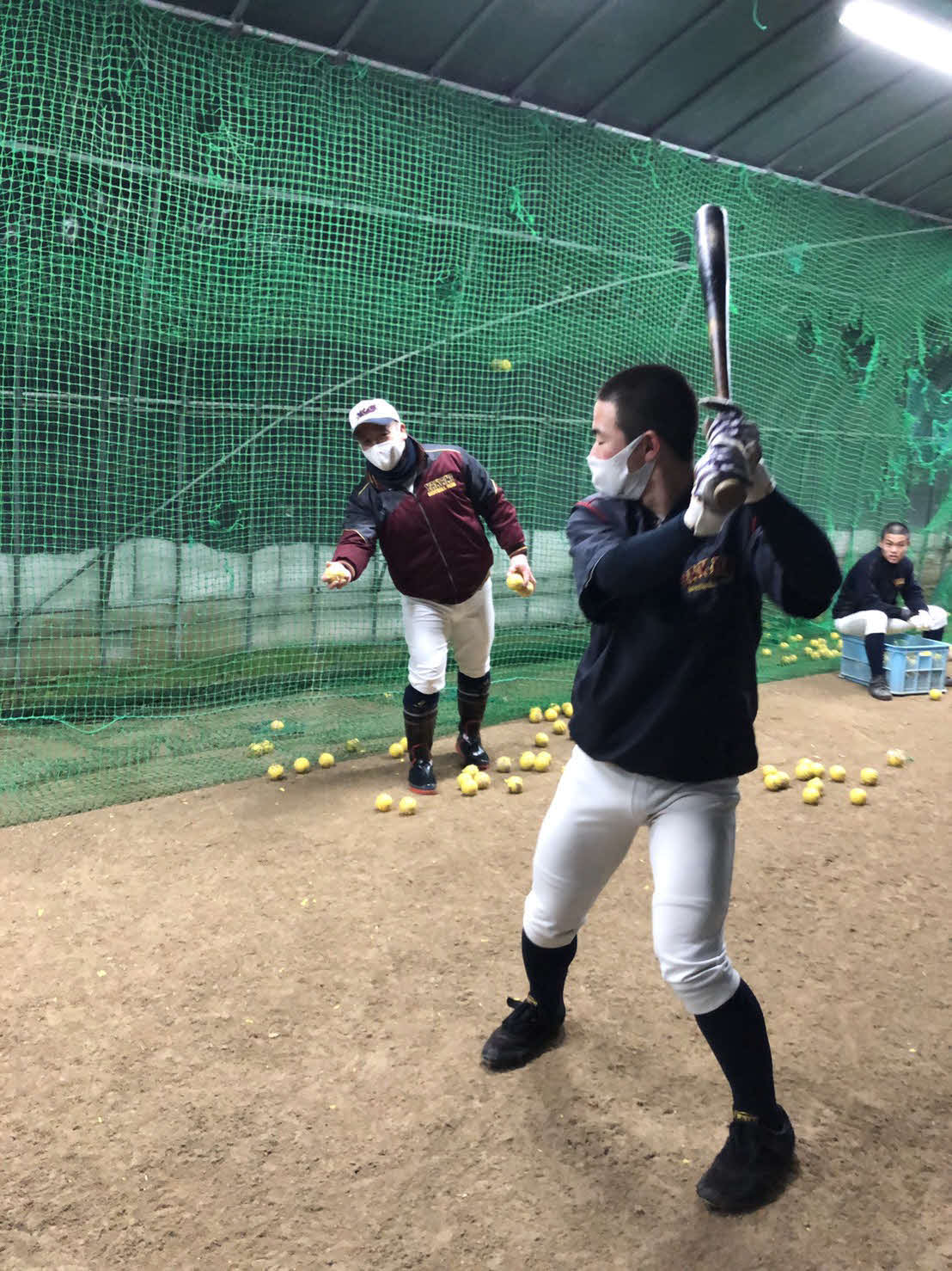 周囲に雪が残った校内のビニールハウスでティー打撃を指導する矢上・山本監督（チーム提供）