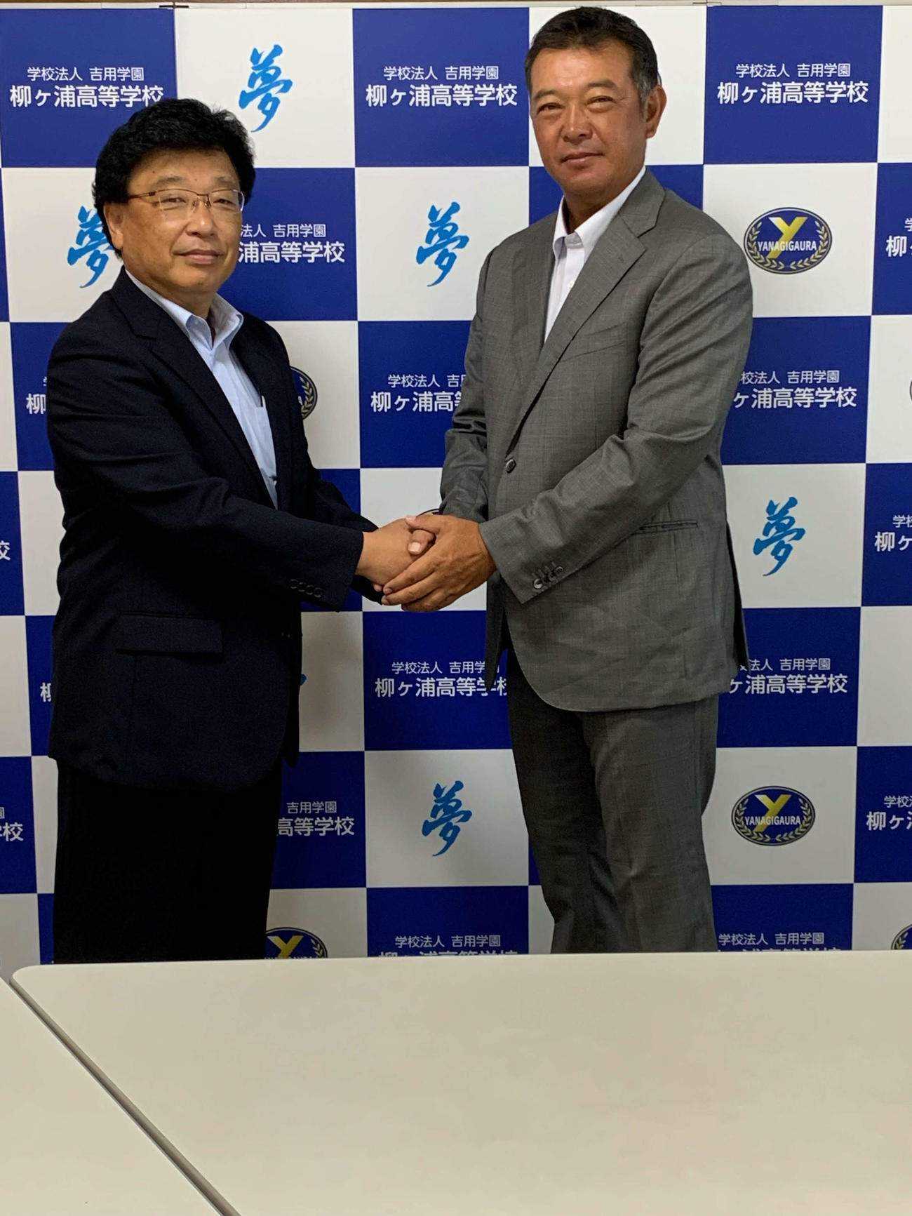 佐藤扇太郎校長（左）と握手を交わす、柳ケ浦の新監督に就任した鈴木聡氏　（学校提供）