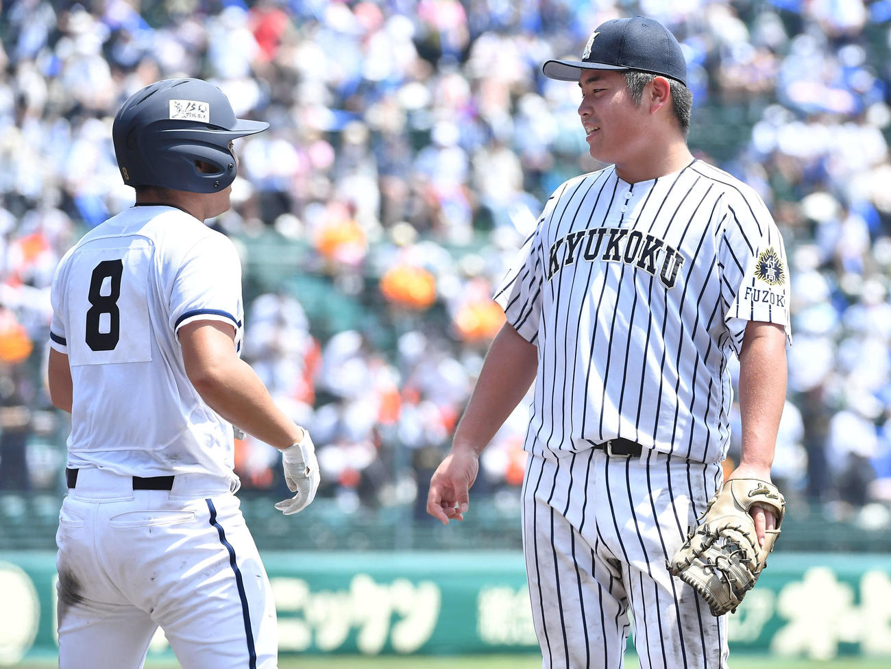 九州国際大付対高松商　4回裏高松商2死一塁、四球で出塁した浅野（左）と話す九州国際大付・佐倉（撮影・岩下翔太）