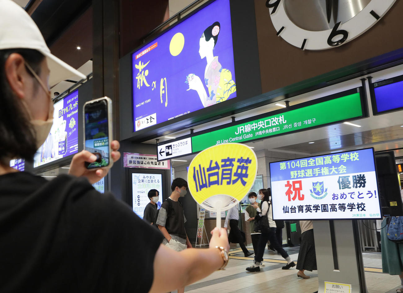 仙台育英のうちわを手に優勝を祝う画面を記念撮影する人