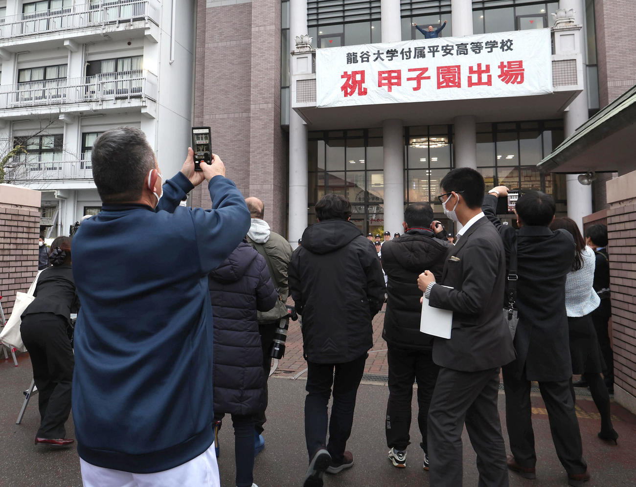 歓喜のガッツポーズする龍谷大平安・川口コーチ（中央後方）をスマートフォンのカメラで撮影する原田監督（左）（撮影・白石智彦）