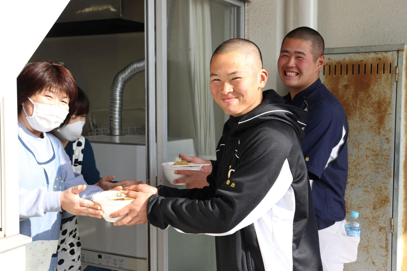 センバツ出場の激励会で、父兄が作ってくれた豚汁うどんと水餃子を受け取る（左から）岩出と小川（撮影・保坂淑子）