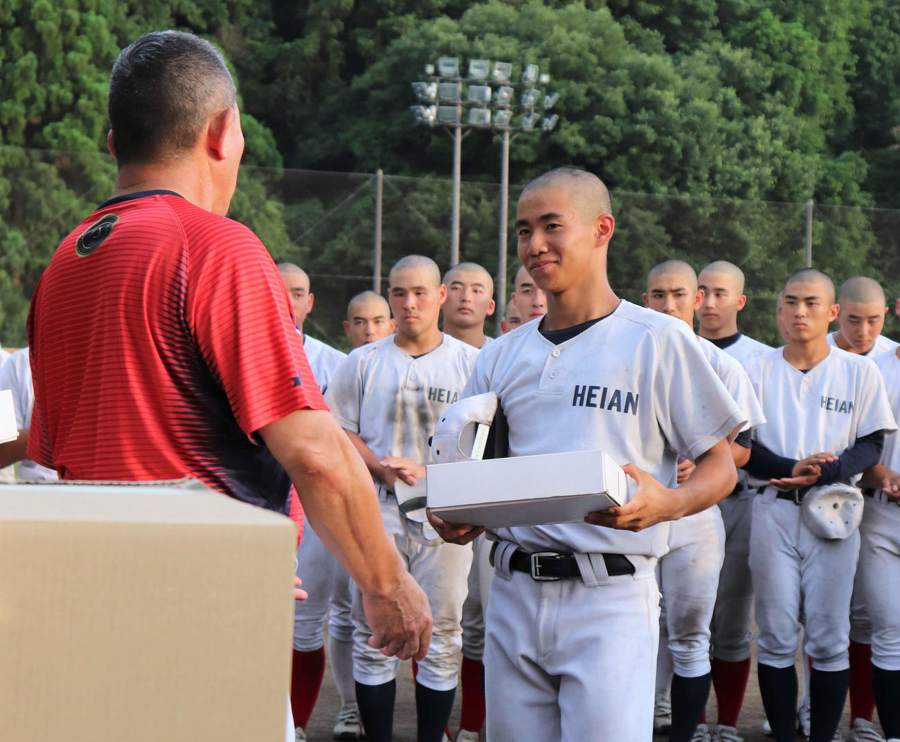 龍谷大平安の原田英彦監督（63）から背番号1のユニホームを手渡される桑江駿成投手（3年）