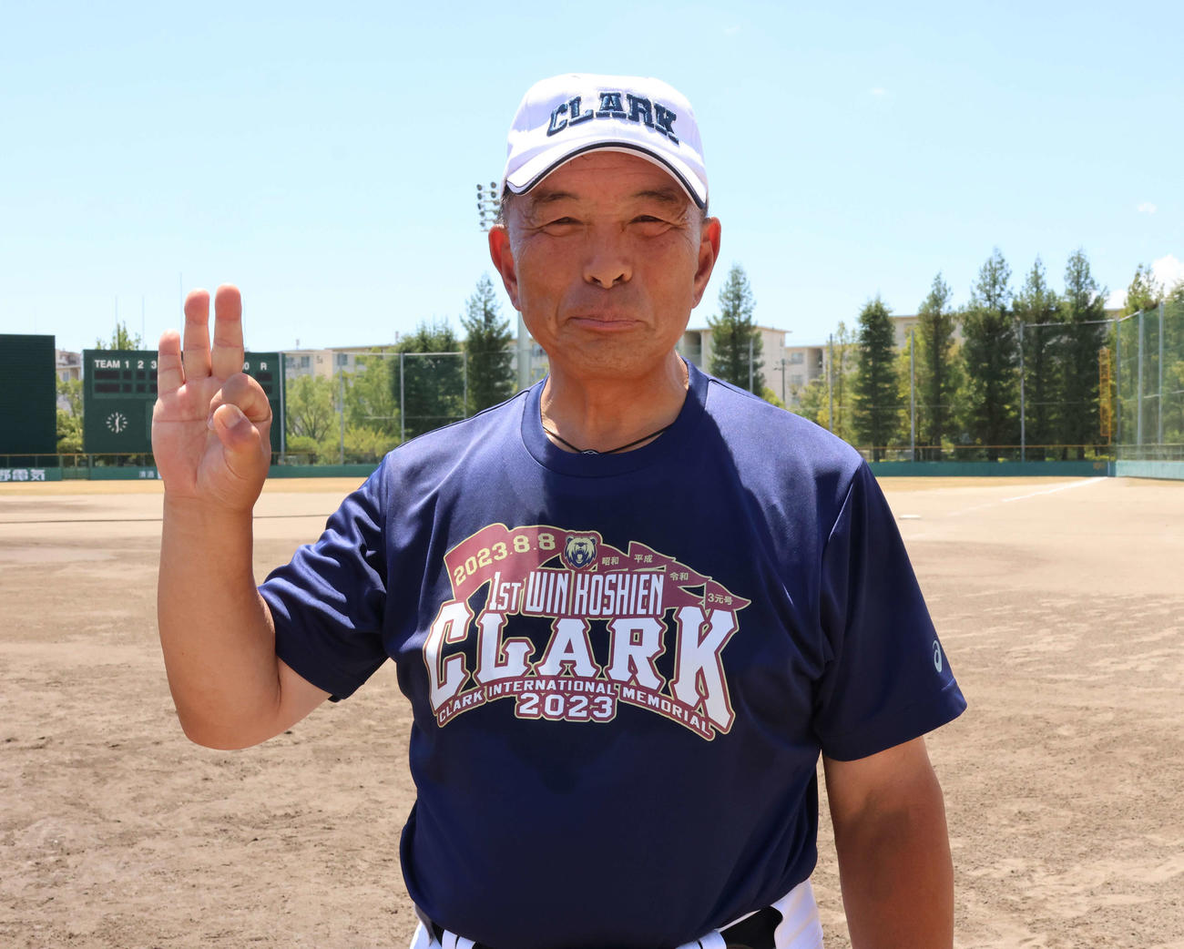 3元号勝利達成の記念Tシャツを着用し、笑顔をみせるクラーク・佐々木監督（撮影・山崎純一）