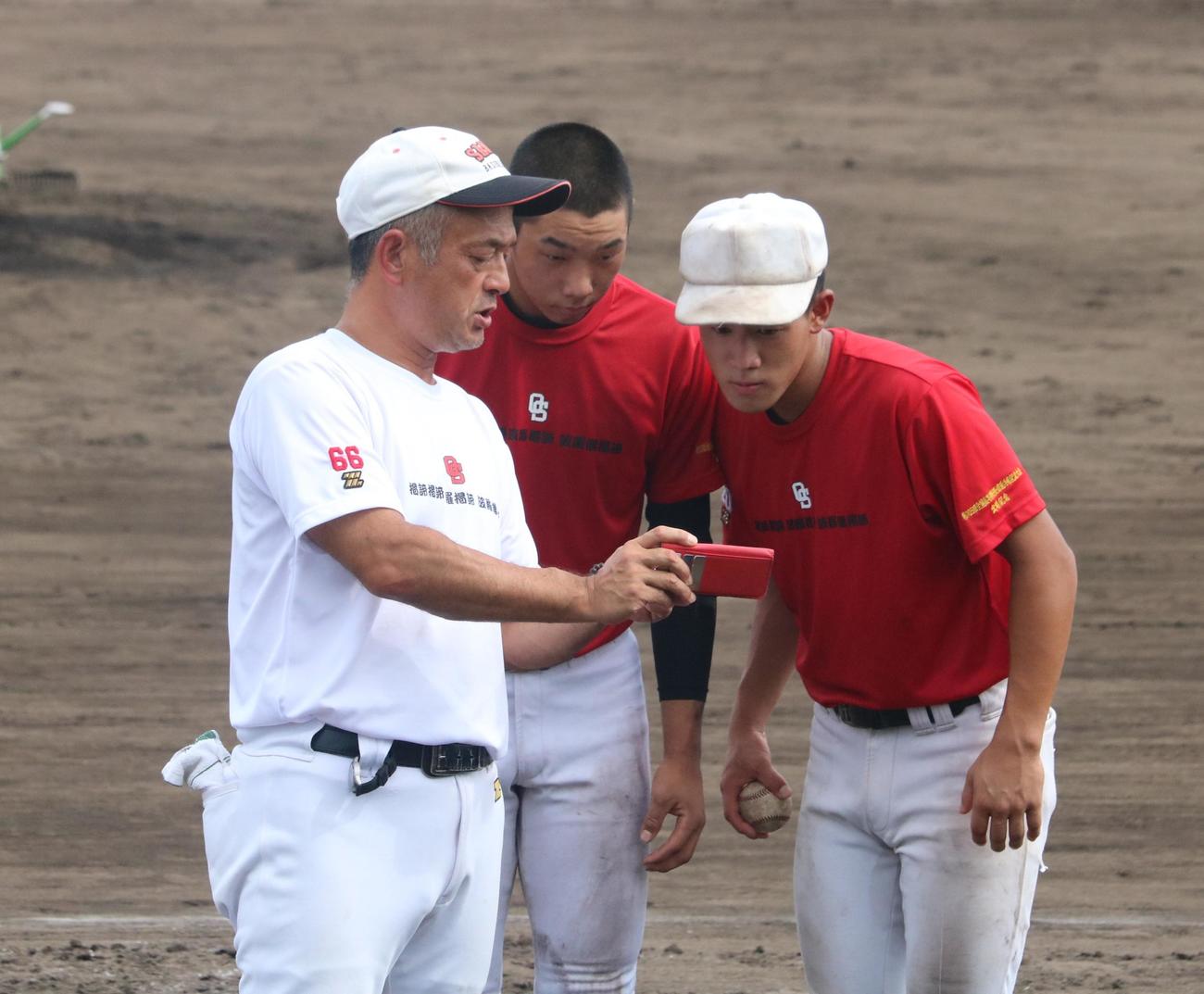 おかやま山陽の堤尚彦監督が田内真翔と藤井潤政のスローイングについてスマホを交えて指導する（撮影・林亮佑）