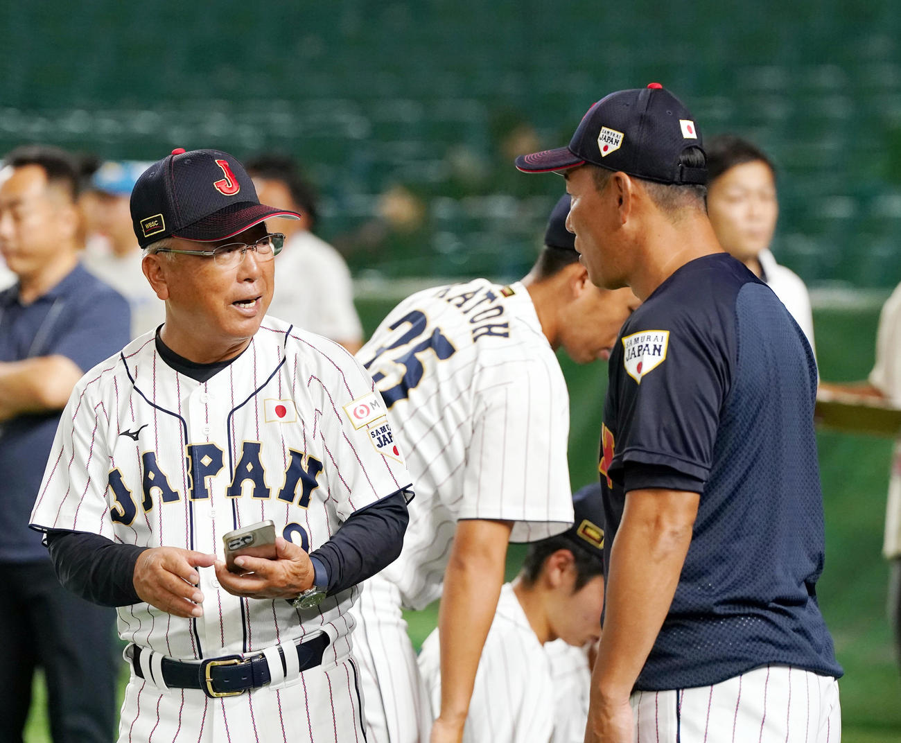 高校日本代表対大学日本代表　試合前に談笑する馬淵監督（左）とU12井端監督（撮影・狩俣裕三）