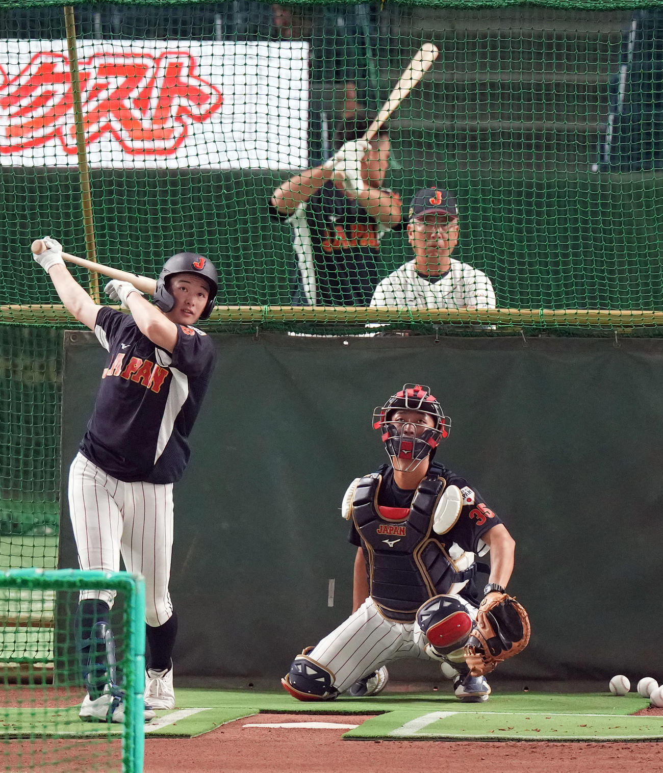 高校日本代表対大学日本代表　試合前の練習で、馬淵監督（後方）が見守る中、フリー打撃を行う丸田（撮影・狩俣裕三）