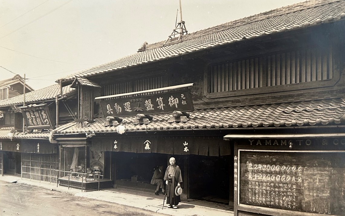 山本商店の店先に立つ山本権十郎。東京6大学野球の試合結果を掲示している（山本宗平さん提供）