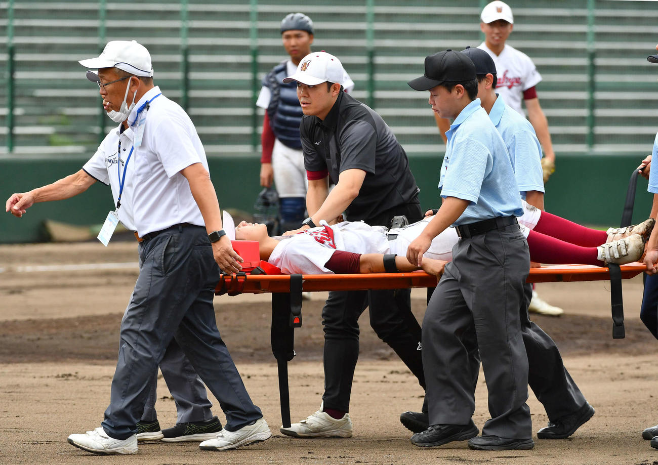 玄界対北九州　6回表玄界1死二塁、平田の打球処理の際に左肩を痛め、担架で運ばれる塚本。右奥は心配そうに見つめる谷元（撮影・岩下翔太）