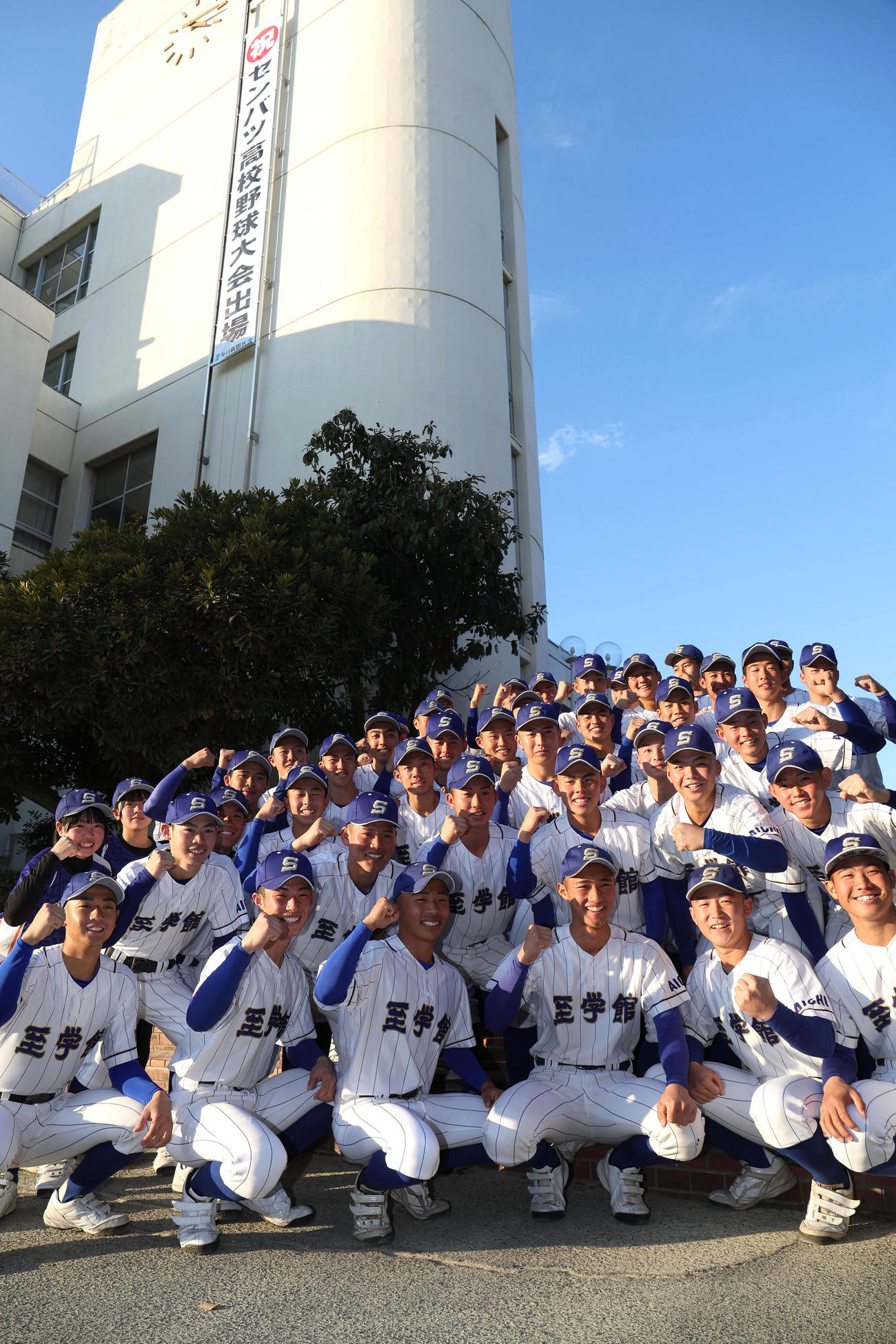 祝センバツ高校野球大会出場の垂れ幕をバックにガッツポーズで記念写真に納まる至学館ナイン（撮影・白石智彦）