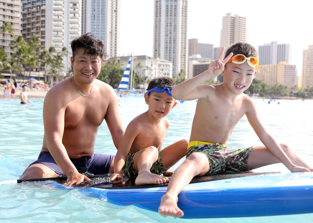 巨人ハワイ優勝旅行　ハワイのビーチでサーフィンにまたがりパパの顔を見せる村田（左）。手前から長男閏哉くん、次男凰晟くん（2014年12月11日撮影）