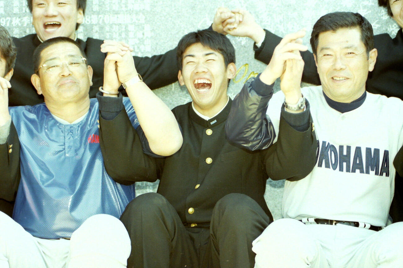99年3月、横浜高校の卒業式を終えた松坂大輔（中央）は、野球部の記念除幕式で渡辺元智監督（右）小倉清一郎部長と手をつないで笑顔