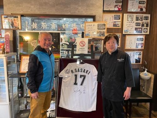 陸前高田市の中華料理店「昇龍厨房四海楼」。佐々木朗希投手のサイン入りユニホームや写真などが飾られている。左は福島良一さん、右は店主の長田正広さん（福島良一さん提供）