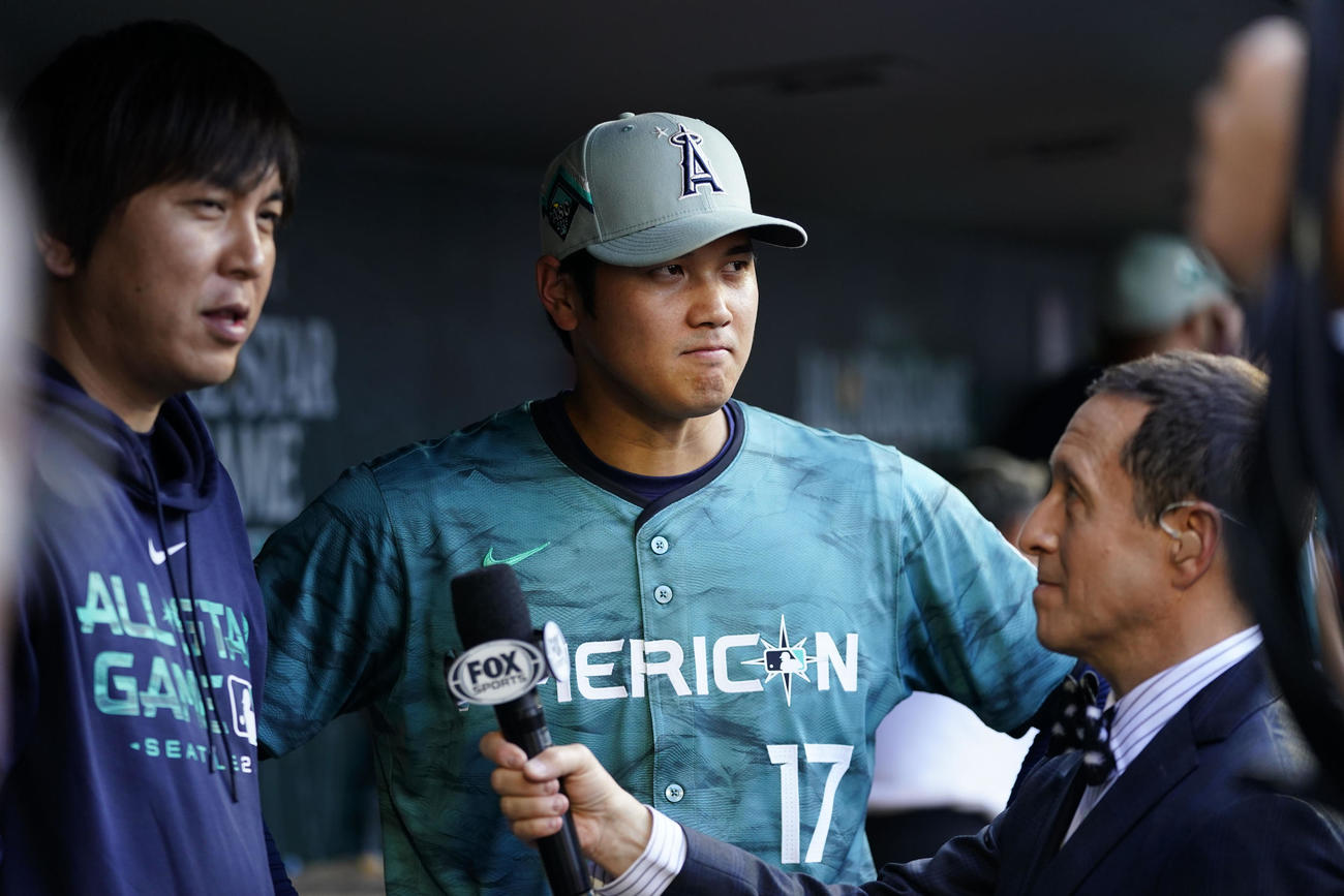 オールスター　ベンチでインタビューを受ける大谷翔平（右）。左は水原通訳（AP)