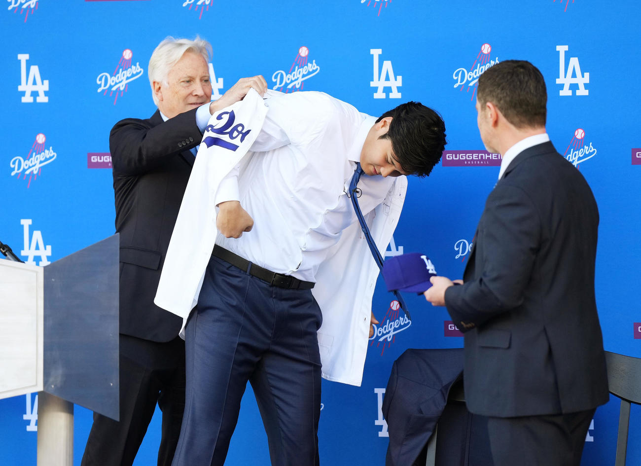 ドジャース入団会見で球団オーナーのウォルター氏（左）にユニホームを着させてもらう大谷。右はフリードマン編成本部長（撮影・菅敏）
