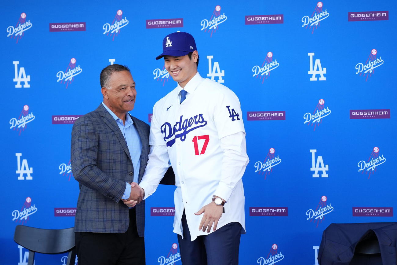 入団会見でドジャースのユニホームに袖を通し、ロバーツ監督と握手を交わす大谷（撮影・菅敏）