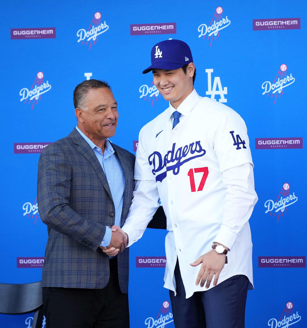 入団会見でドジャースのユニホームに袖を通し、ロバーツ監督と握手を交わす大谷（撮影・菅敏）