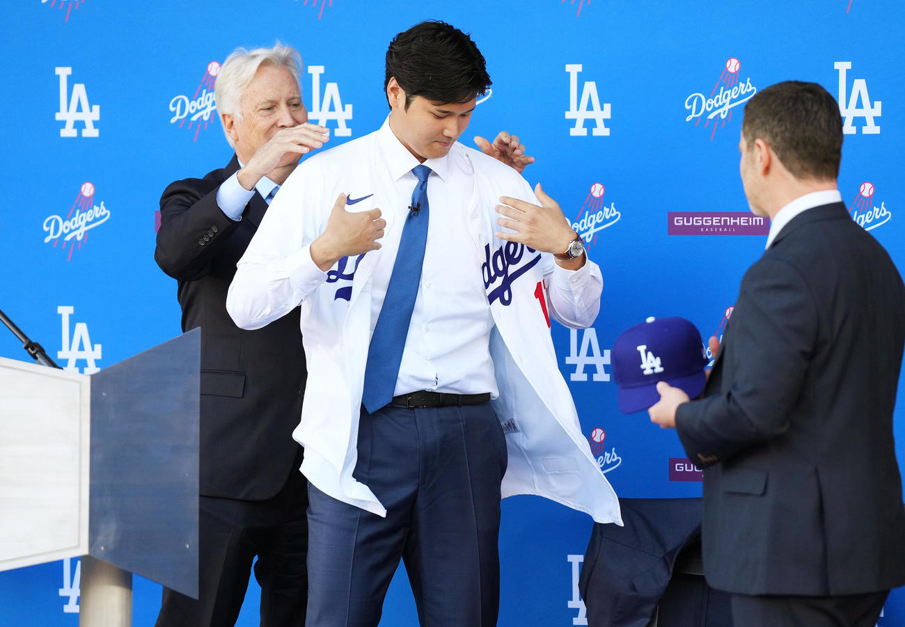 ドジャース入団会見で球団オーナーのウォルター氏（左）にユニホームを着させてもらう大谷。右はフリードマン編成本部長（撮影・菅敏）