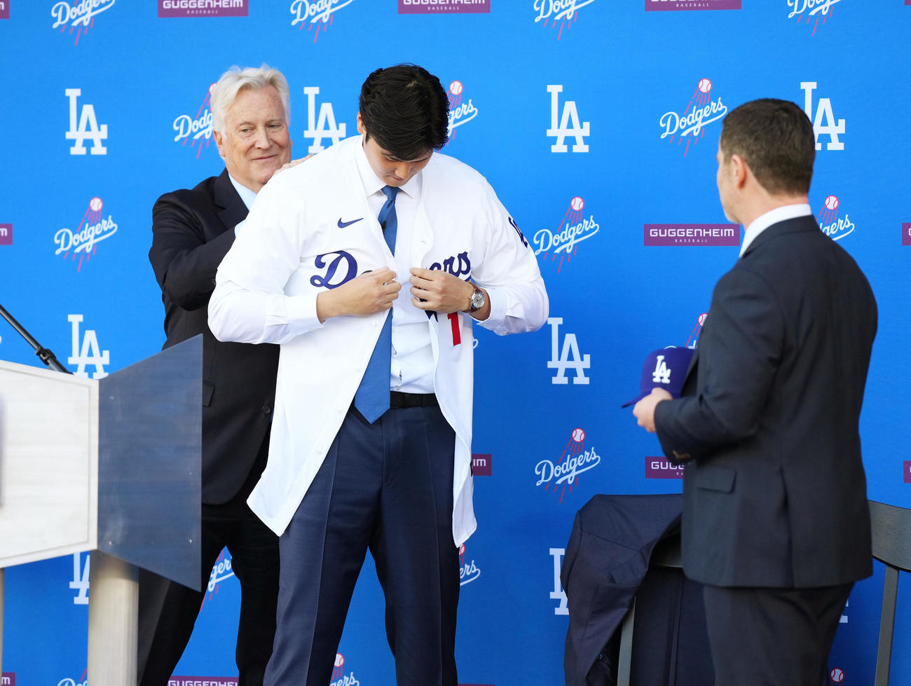 ドジャース入団会見で球団オーナーのウォルター氏（左）にユニホームを着させてもらう大谷。右はフリードマン編成本部長（撮影・菅敏）