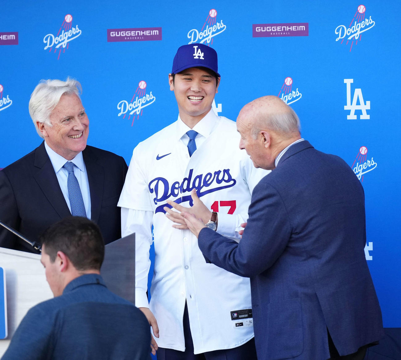 ドジャース入団会見でユニホームに袖を通し笑顔を見せる大谷翔平。左はマーク・ウォルターオーナー、手前右はスタン・カステン球団社長（撮影・菅敏）
