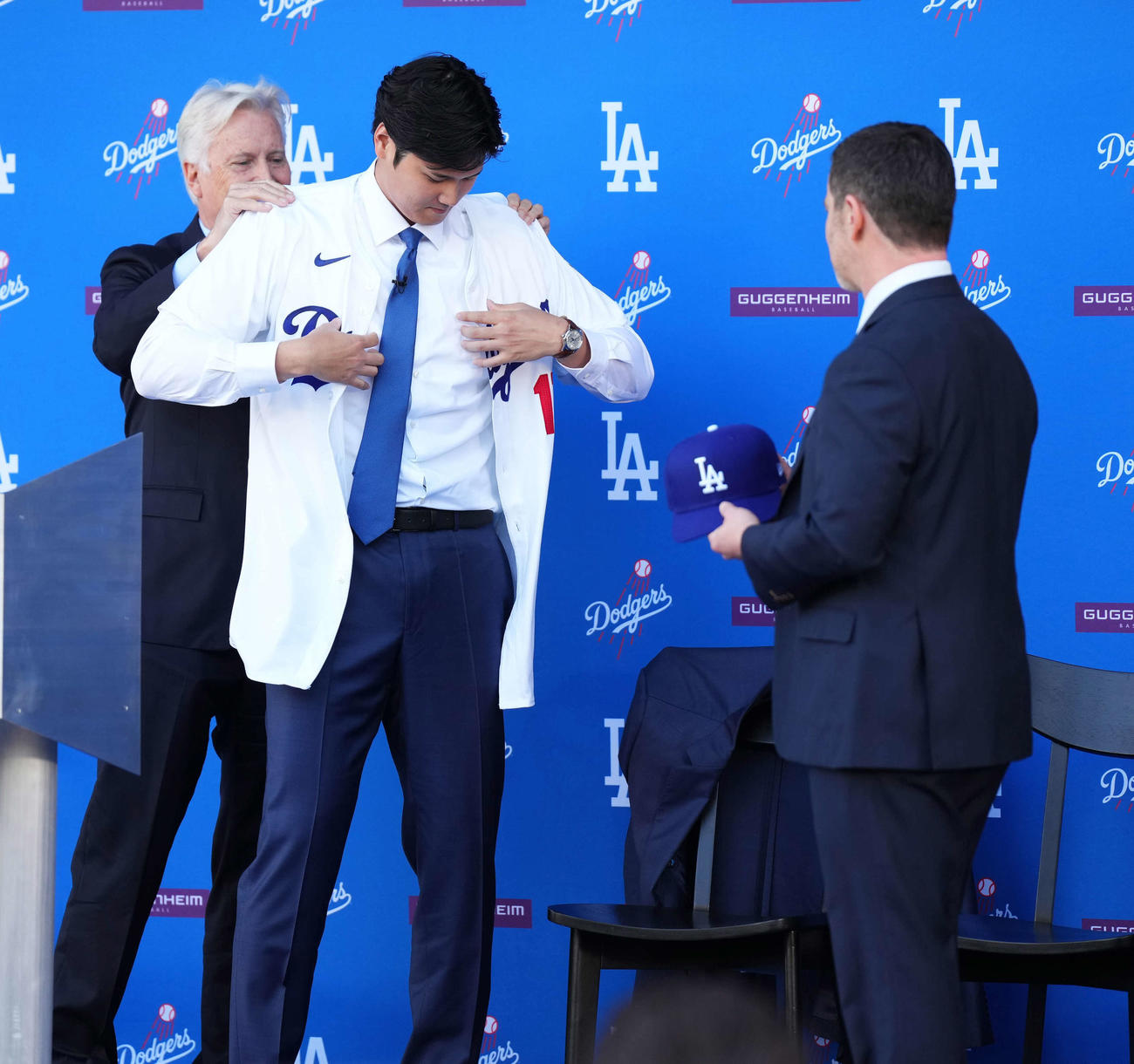 入団会見でドジャースのユニホームに袖を通す大谷。後方左はウォルターオーナー、右はフリードマン編成本部長（撮影・菅敏）