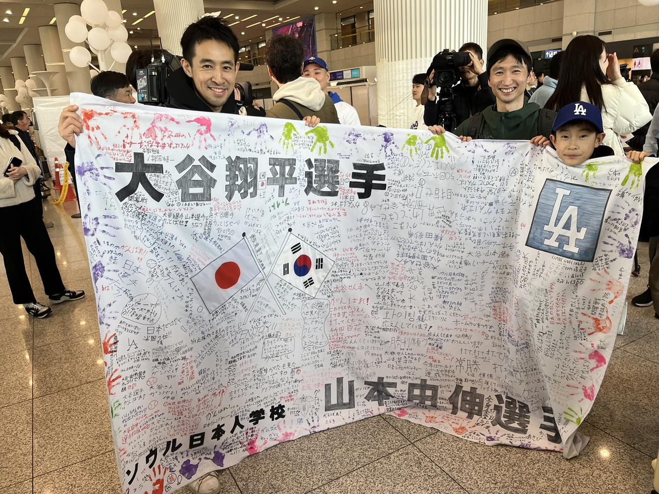 ソウルの日本人学校教師の清水祐輔さん（左）と5年生の泰正さん（右）親子は、生徒が書いた寄せ書きを持って、仁川国際空港第にドジャースナインを出迎えた（撮影・斎藤直樹）