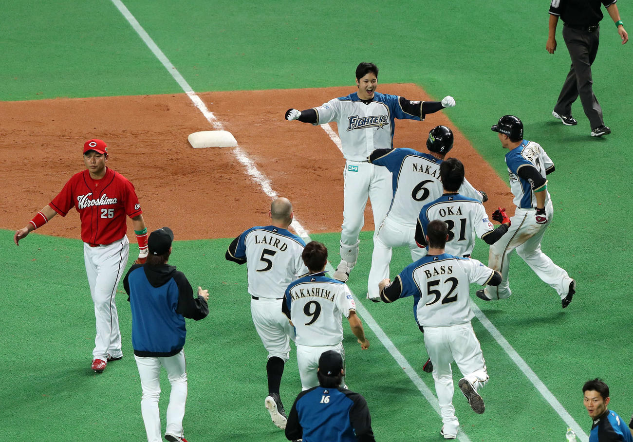 日本ハム対広島　10回裏日本ハム2死二塁、右前にサヨナラ打を放った大谷（後方）は駆け出してきたナインにガッツポーズで応える。左端はがっくりと引き揚げる新井（2016年10月25日撮影）