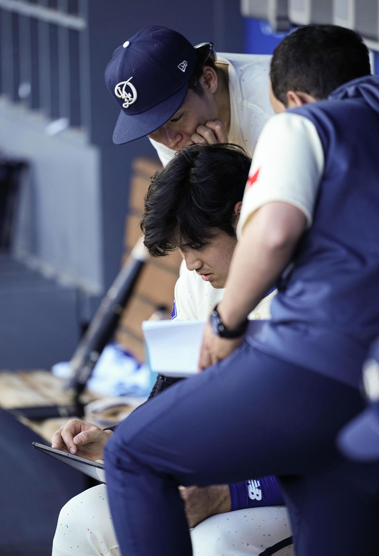 ブルワーズ戦のベンチでタブレット端末を見る大谷翔平。奥は山本由伸（共同）