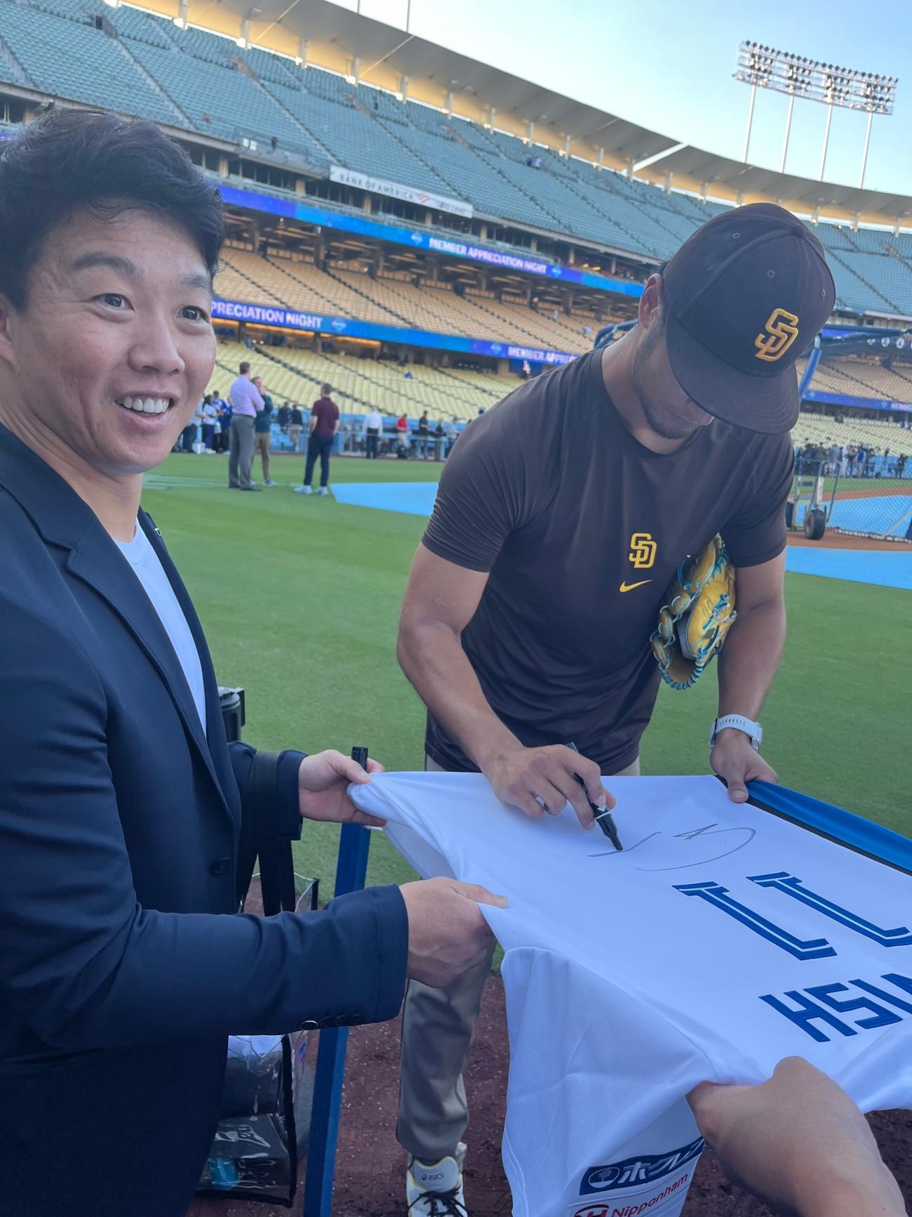 ドジャース－パドレスの試合前、鶴岡慎也氏（左）が持参した日本ハムのユニホームにサインするパドレス・ダルビッシュ有投手